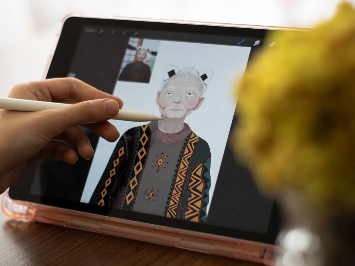 A stylus drawing a character portrait of an older person in a patterned sweater on a tablet screen.