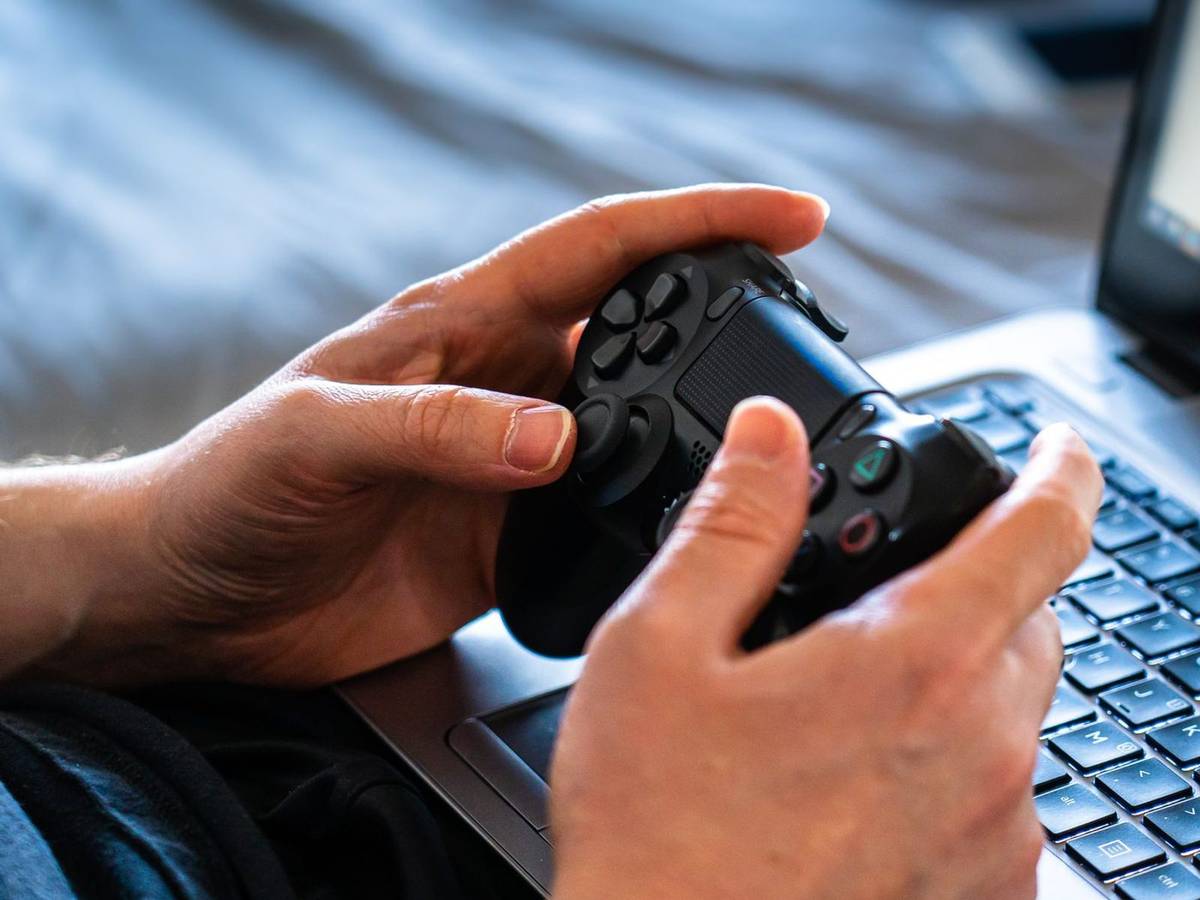 Two hands gripping a black game controller held over an open laptop keyboard.