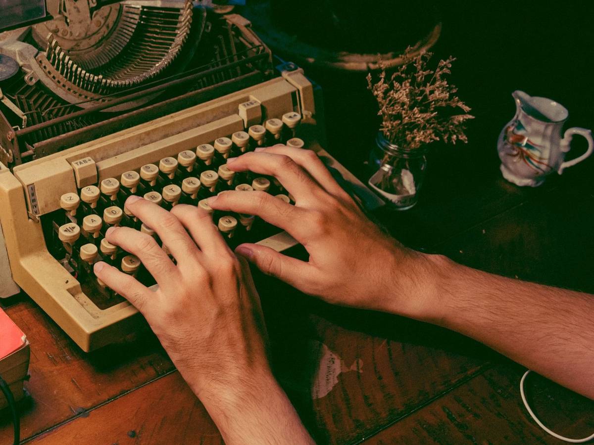 Two hands typing on a cream vintage typewriter on a wooden desk.