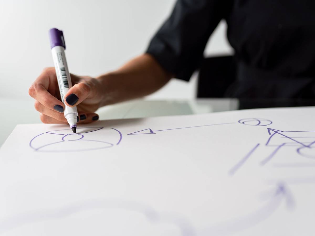 A hand drawing a diagram of circles, arrows and triangles in purple marker on a large white sheet.