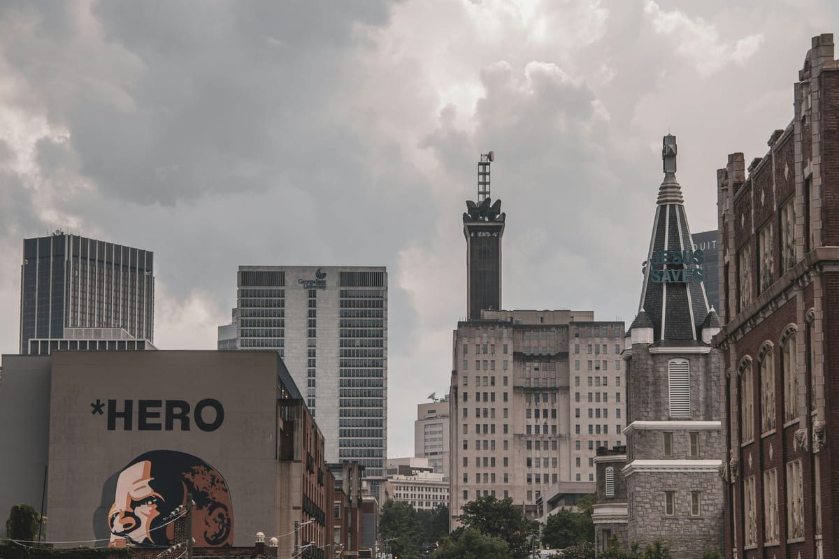 Downtown towers and older stone buildings under a gray sky, with a painted mural in front