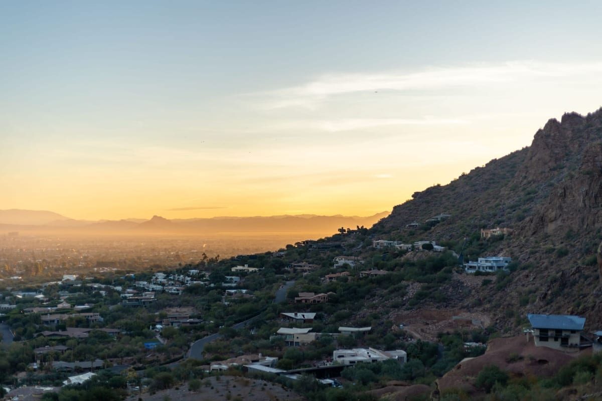 Sunset over a wide valley seen from a rocky hillside, with houses spread below