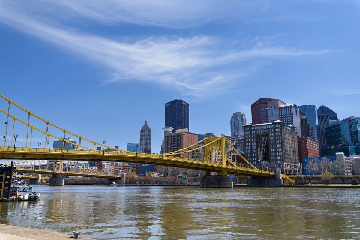 A yellow suspension bridge over a river, with downtown towers behind
