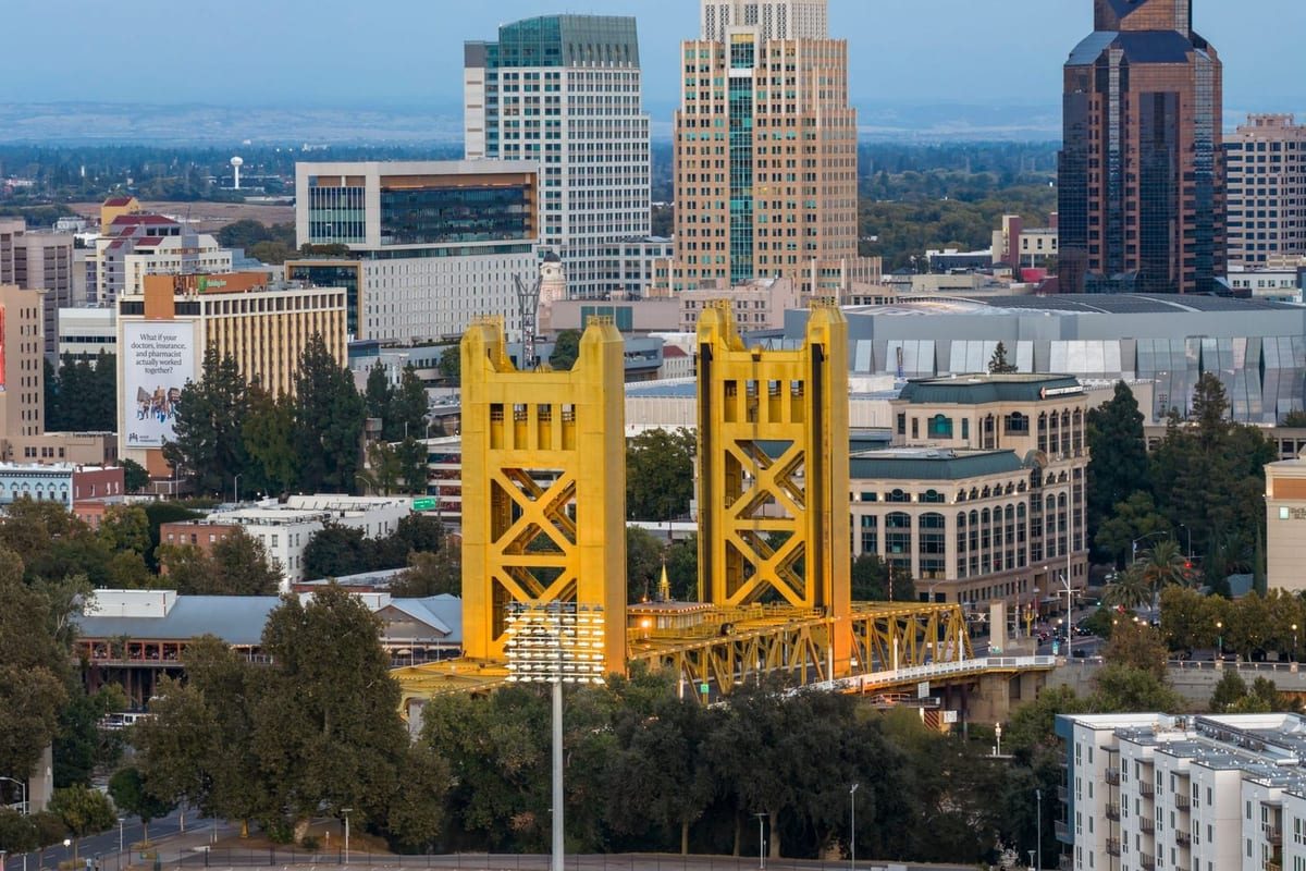 A gold vertical-lift bridge in front of a cluster of downtown towers, with trees and low buildings below