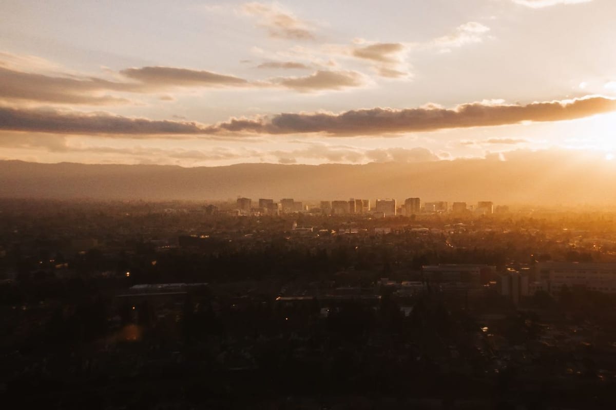 A low skyline under golden sunset haze, seen across a dark spread of trees
