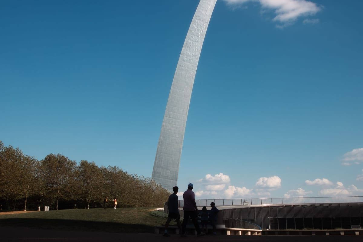 A tall stainless-steel arch against a blue sky, with people silhouetted on a walkway