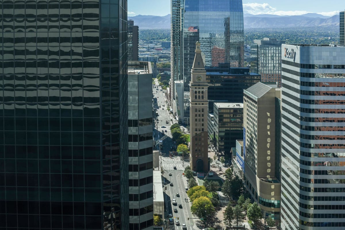 Looking down a downtown street between dark glass towers, mountains faint on the horizon