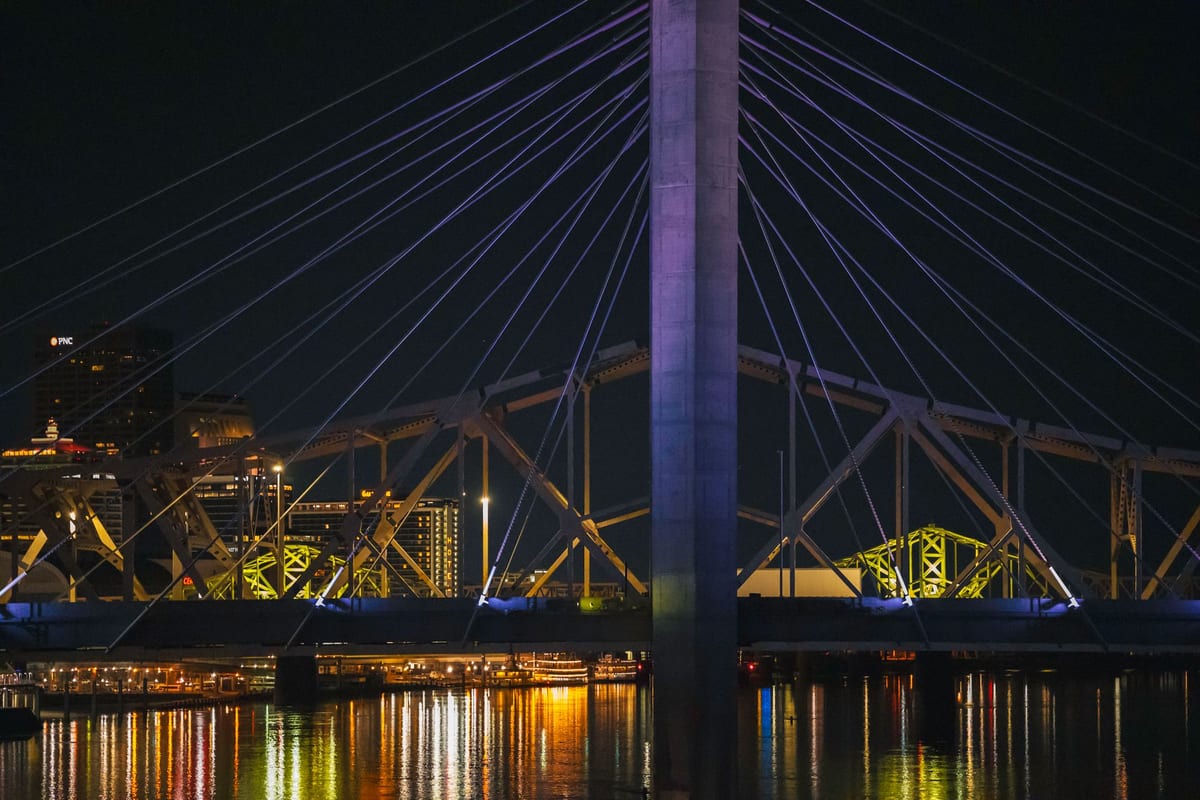 A cable-stayed bridge lit purple at night above a river reflecting city lights