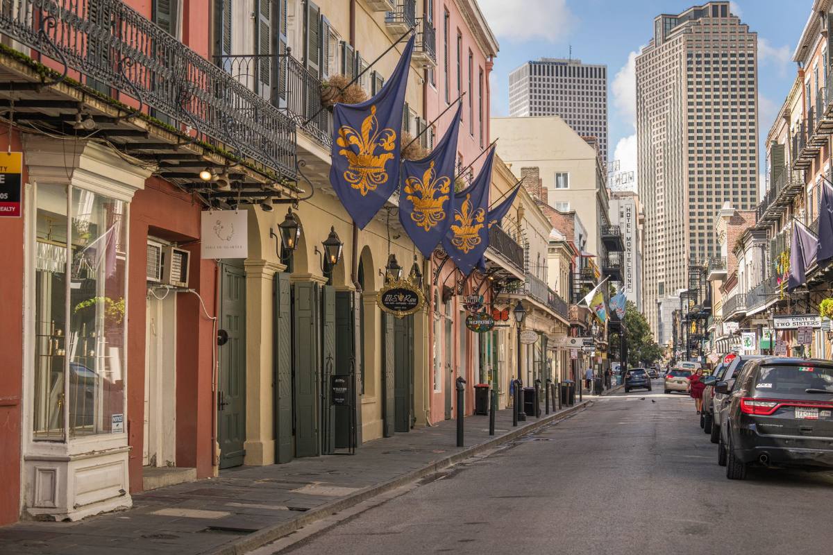 A street of iron balconies and hanging banners, with office towers rising at the far end