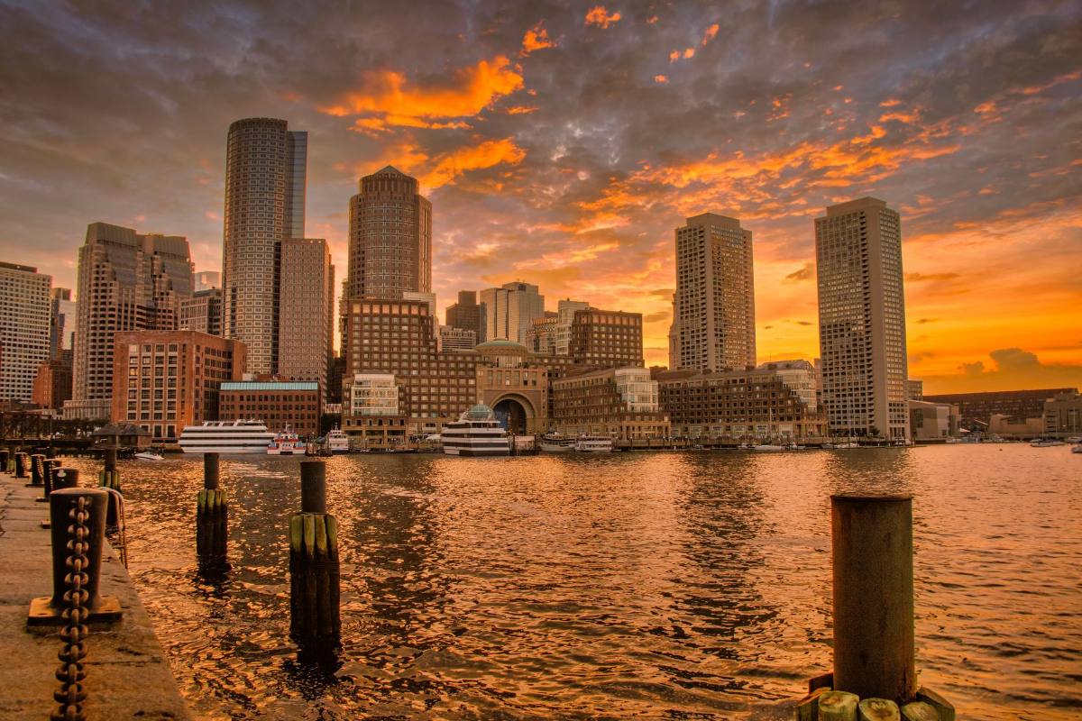 A waterfront skyline under an orange sunset, old pier posts standing in the water