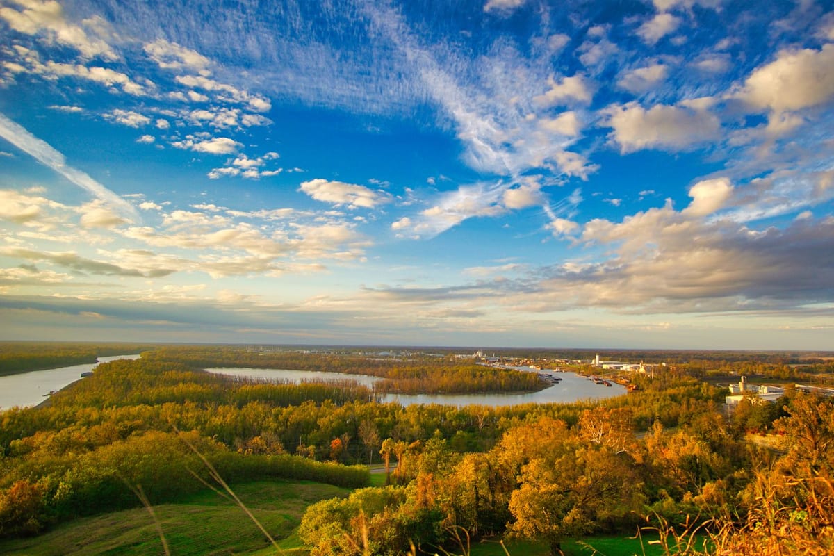 A wide river winding through autumn woods under a sky of streaked clouds