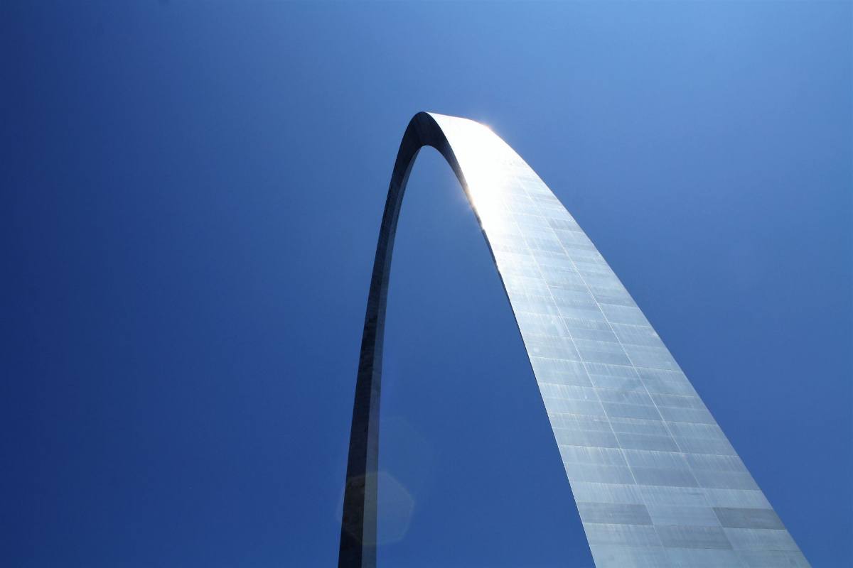 A polished steel arch rising into a deep blue sky, seen from directly below