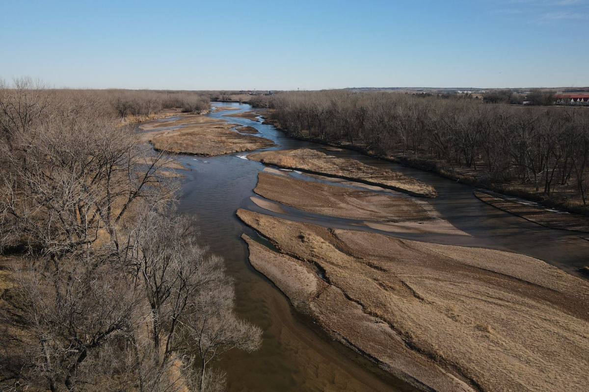 A wide, shallow river braided around sandbars, bare trees along its banks