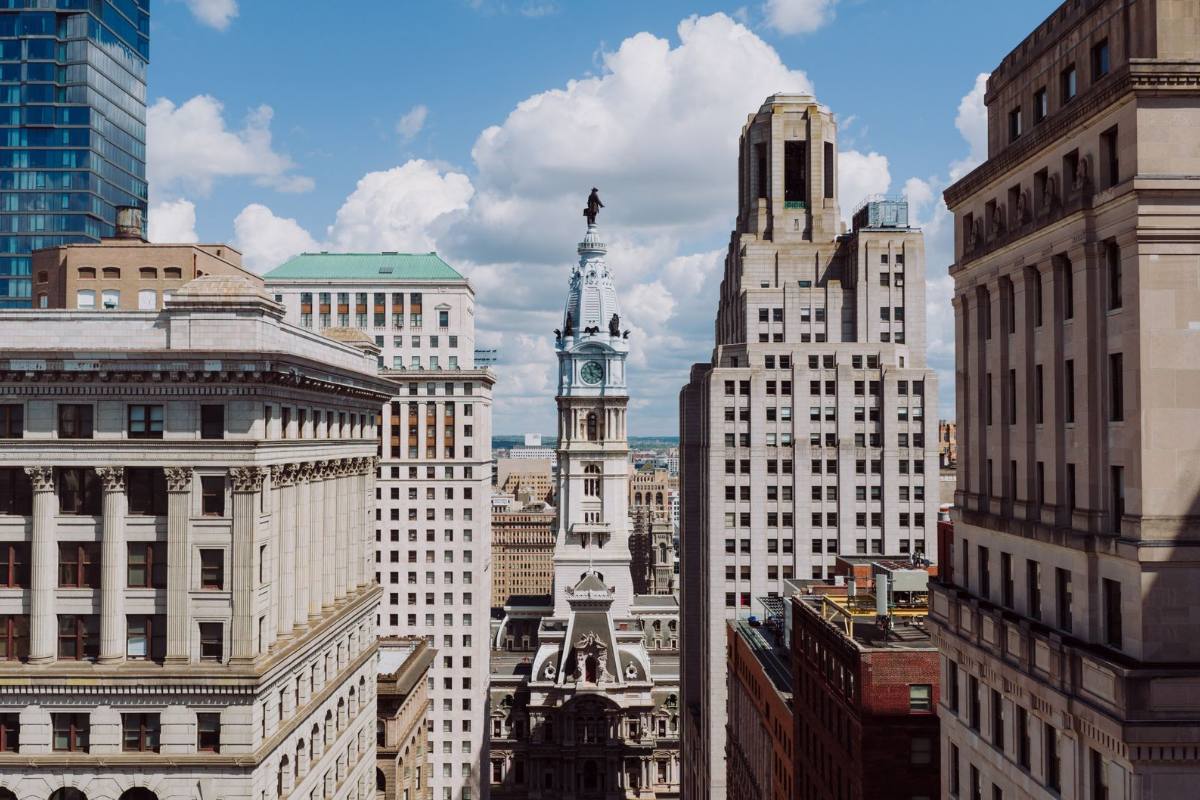 An ornate clock tower between stone office buildings, seen from street level