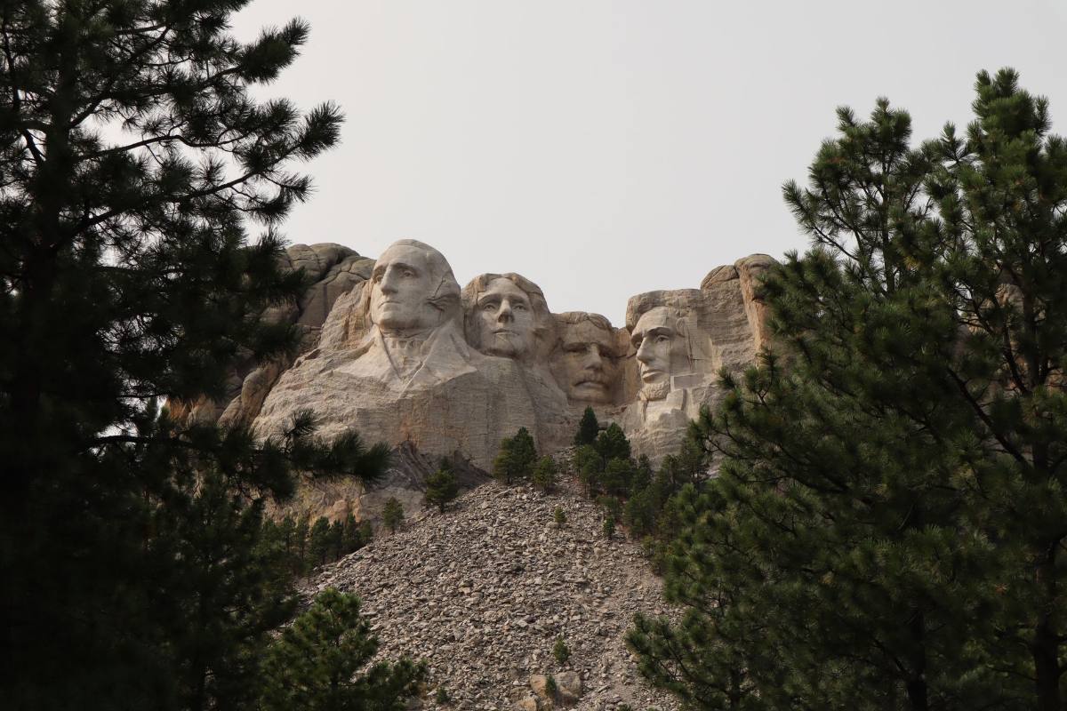 Carved stone faces on a granite cliff, seen between tall pine trees