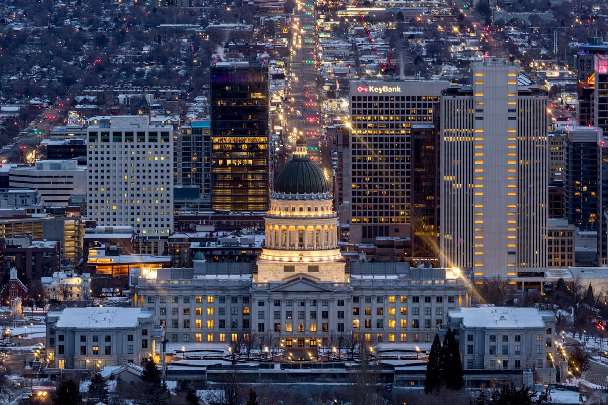 A domed capitol building lit at night at the head of a street of city lights